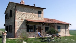 A stone house with a red-tiled roof, a covered patio with chairs, and a garden path. - Villa Sarta - Tuscan country villa with private pool (Pienza)