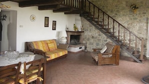 A rustic interior with a stone wall, wooden staircase, a sofa, a table with a glass bowl, and a fireplace. - Villa Sarta - Tuscan country villa with private pool (Pienza)