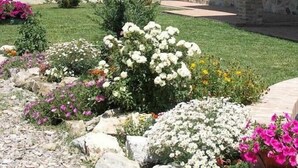 A stone house with a tiled roof, surrounded by a well-maintained garden with various plants and flowers. - Villa Sarta - Tuscan country villa with private pool (Pienza)