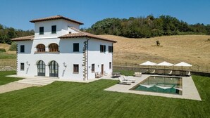 A white villa with a swimming pool, outdoor seating, and a view of a hill. - Villa San Francesco - Private villa with pool (Pian di Scò)