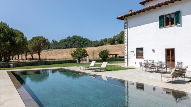 A poolside area with lounge chairs and a dining setup, surrounded by a white building with green shutters, set against a hillside backdrop. - Villa San Francesco - Private villa with pool (Pian di Scò)