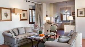 A living room with a sofa, armchair, and coffee table, a kitchen in the background, and framed pictures on the walls. - Villa San Francesco - Private villa with pool (Pian di Scò)