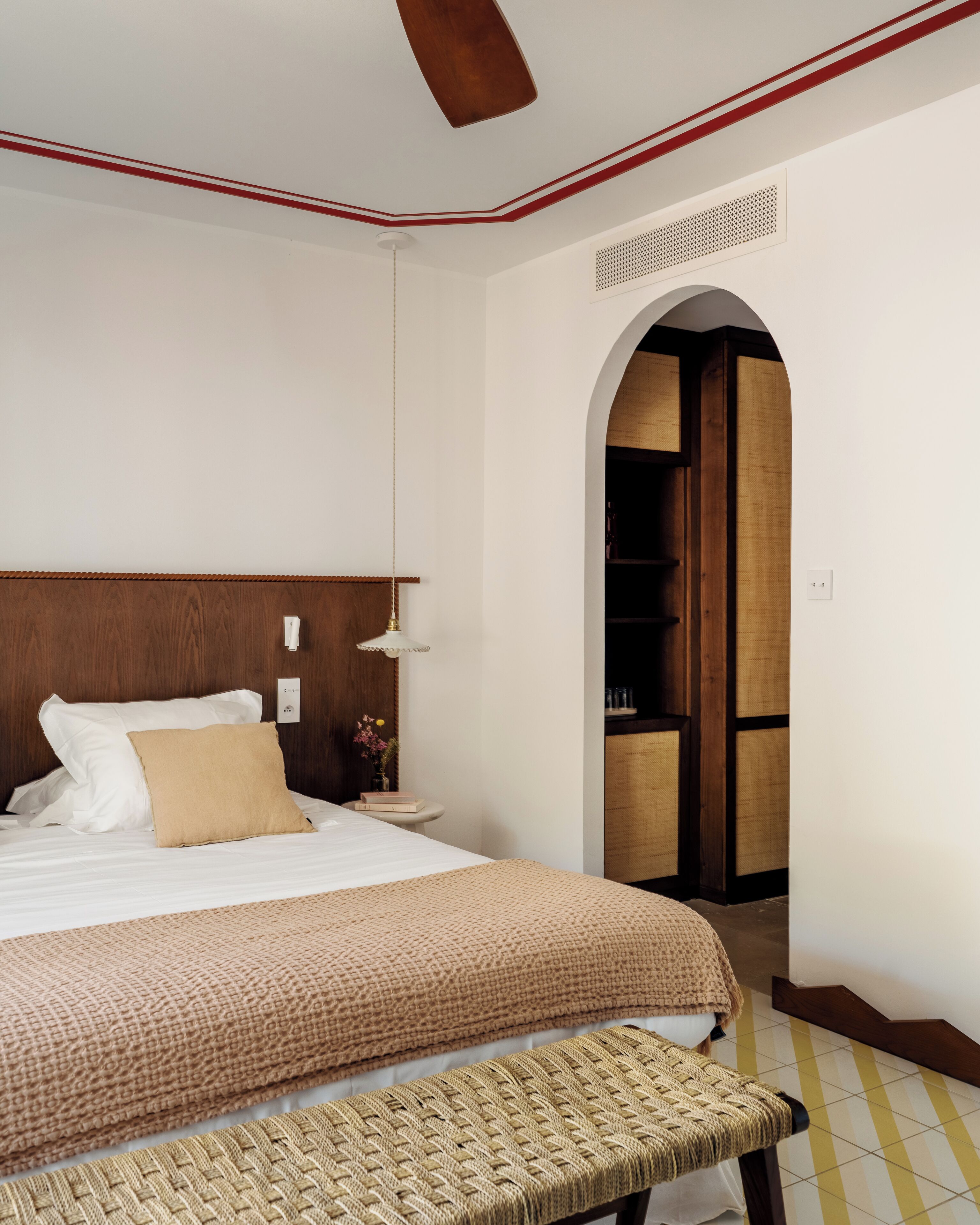 Habitación de hotel impecable, con una cama grande, una mesita de noche con lámpara, y un banco al pie de la cama.