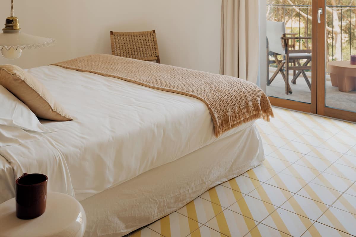 Un dormitorio con cama, mesita de noche, lámpara colgante, ventana con cortinas y vistas al exterior.