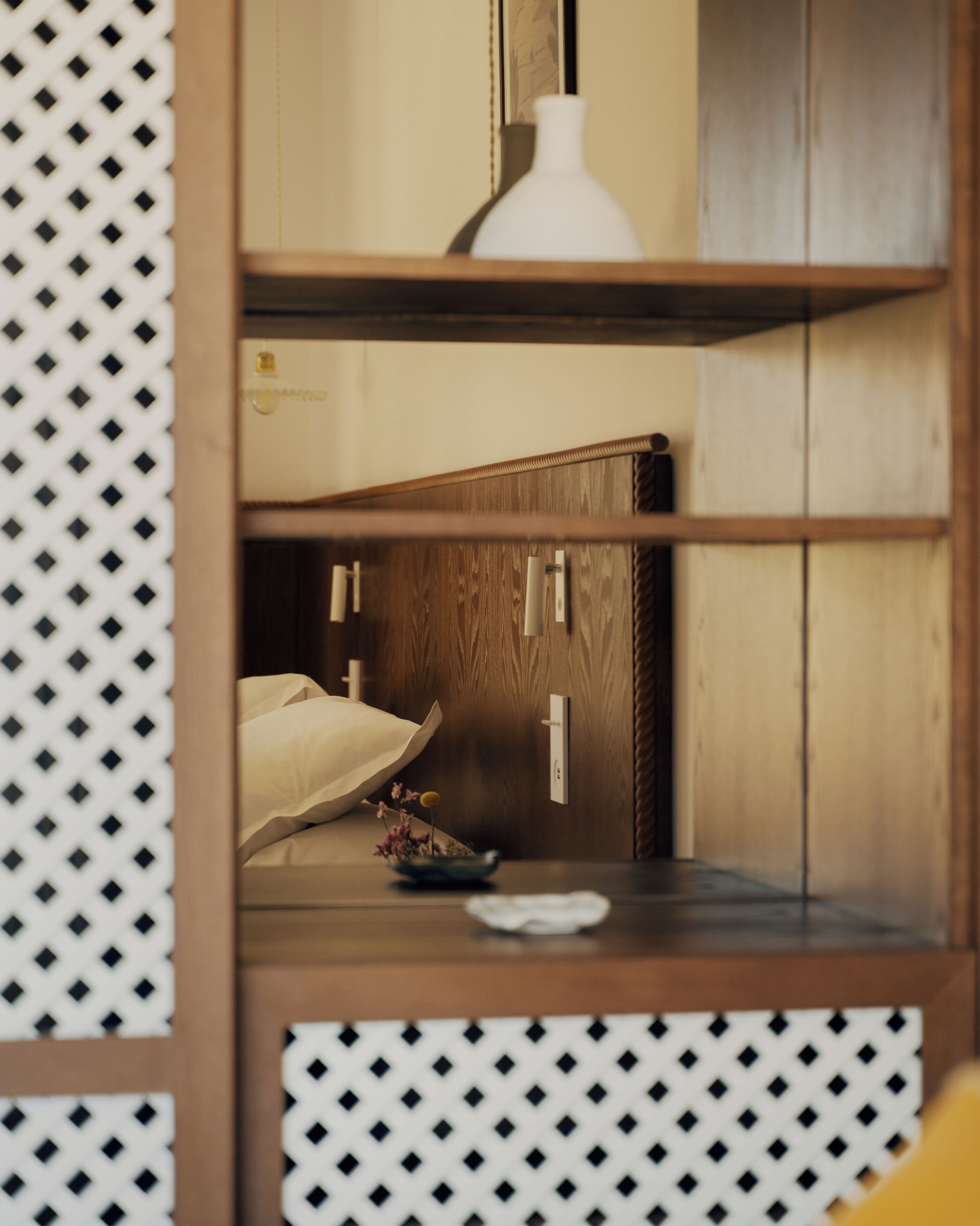 Una habitación con un armario de madera, una cama con almohada blanca y una mesita con un florero y flores.