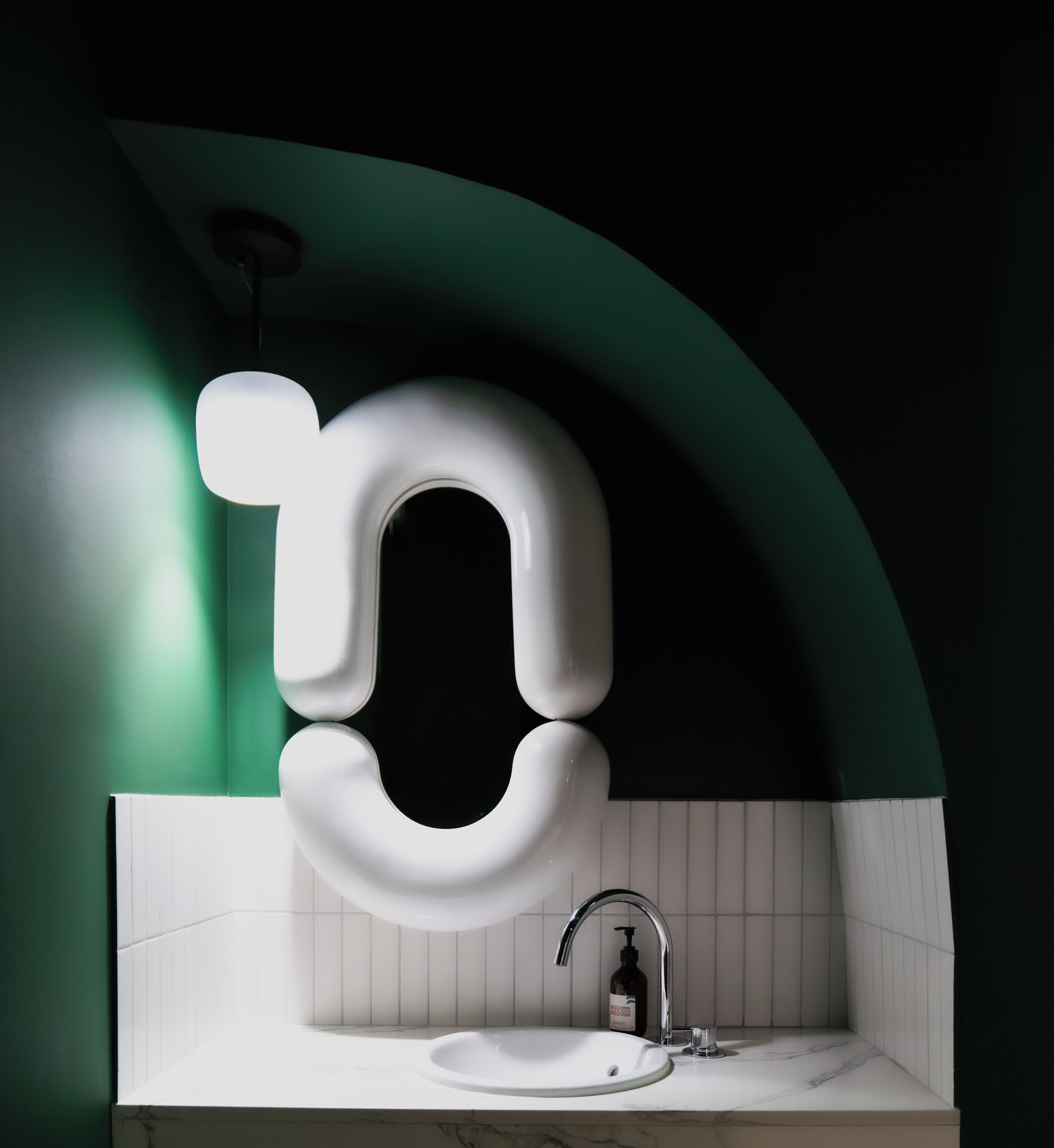 A modern bathroom with a white sink, a chrome faucet, and a green accent wall.