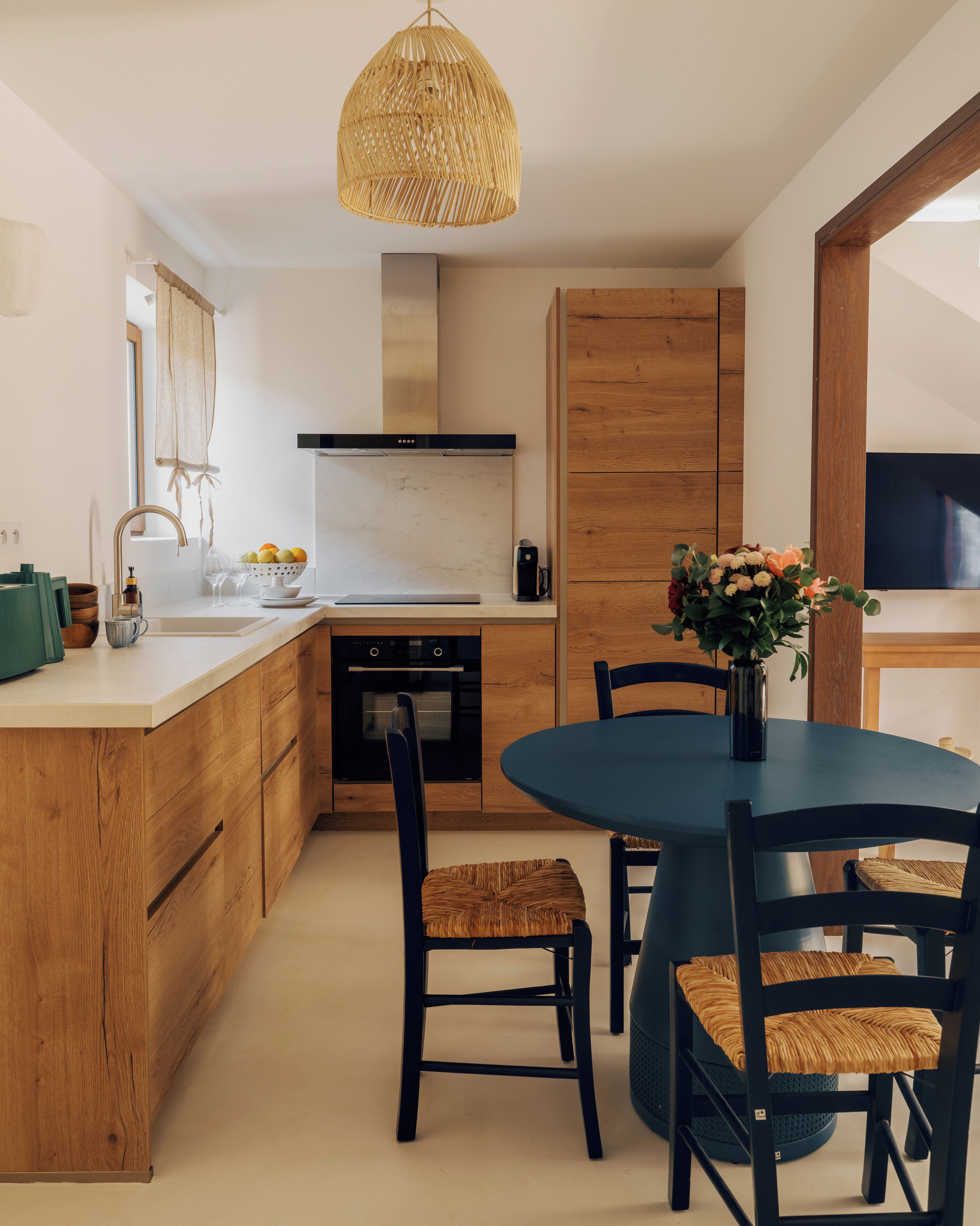 A modern kitchen with wooden cabinets, a central island, a round dining table with chairs, and a hanging light fixture.