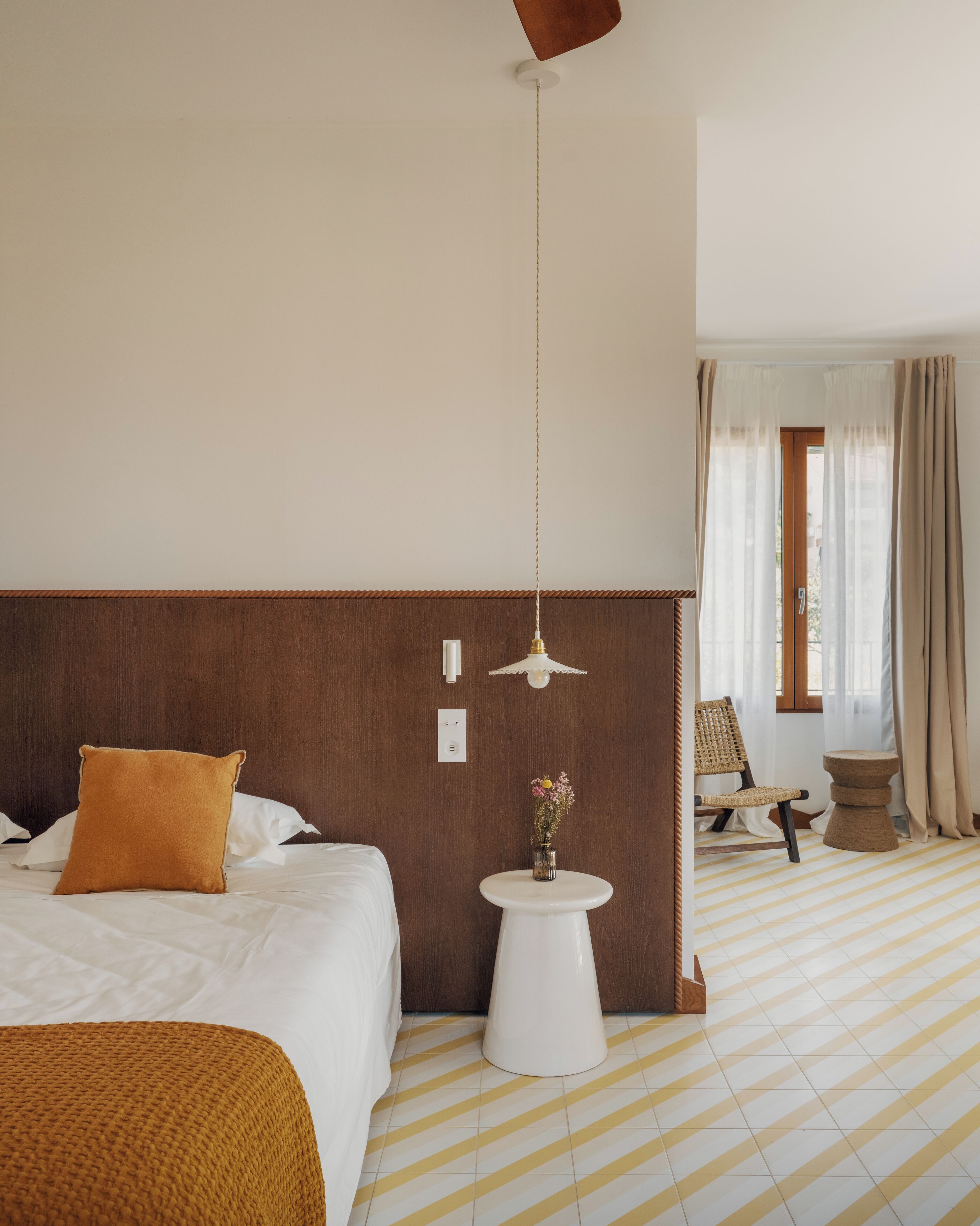 Een hotelkamer met een groot bed, een nachtkastje met een bloevas, een stoel en uitzicht buiten door een raam.