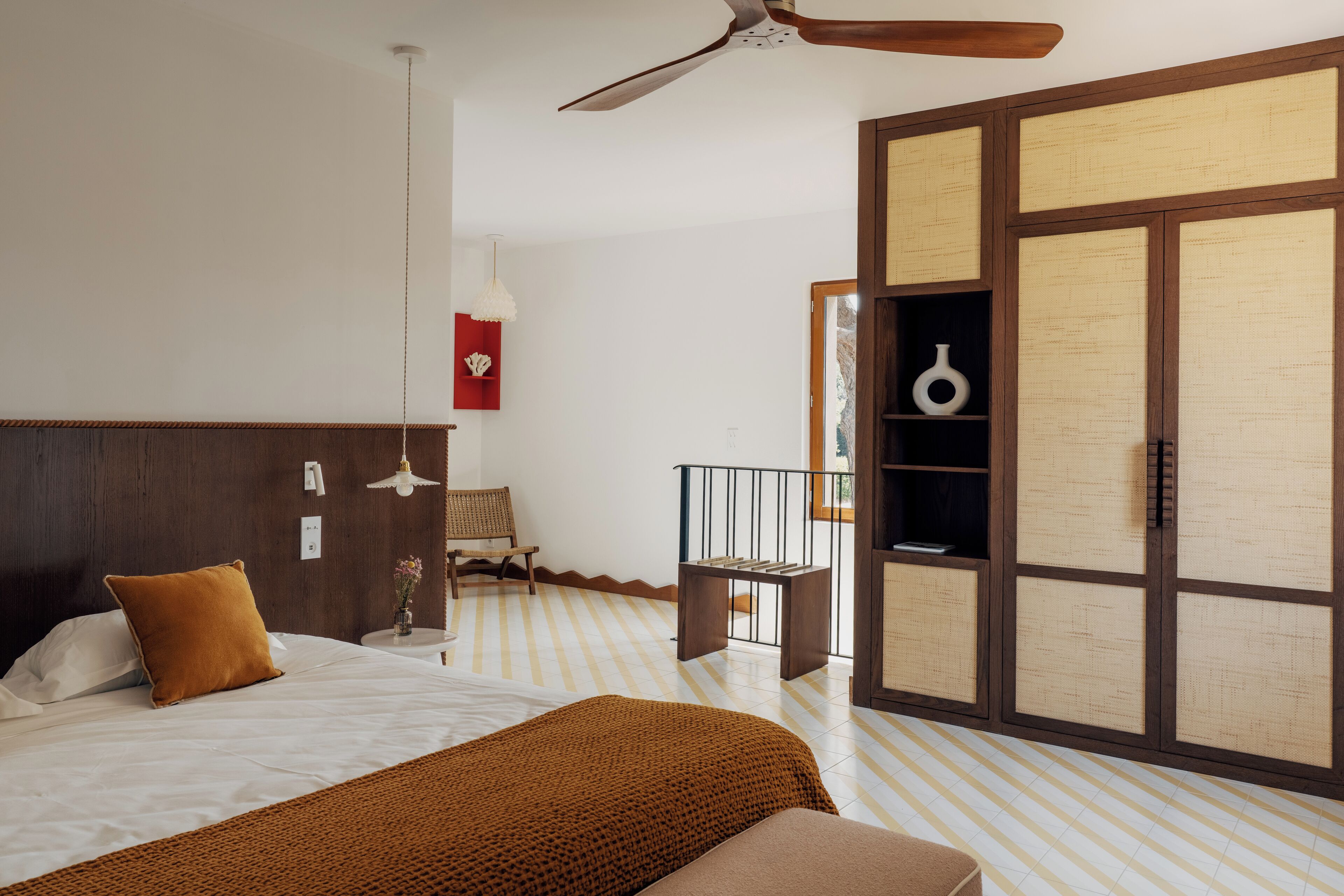 A bedroom with a bed, a ceiling fan, a wooden wardrobe, and a striped floor.