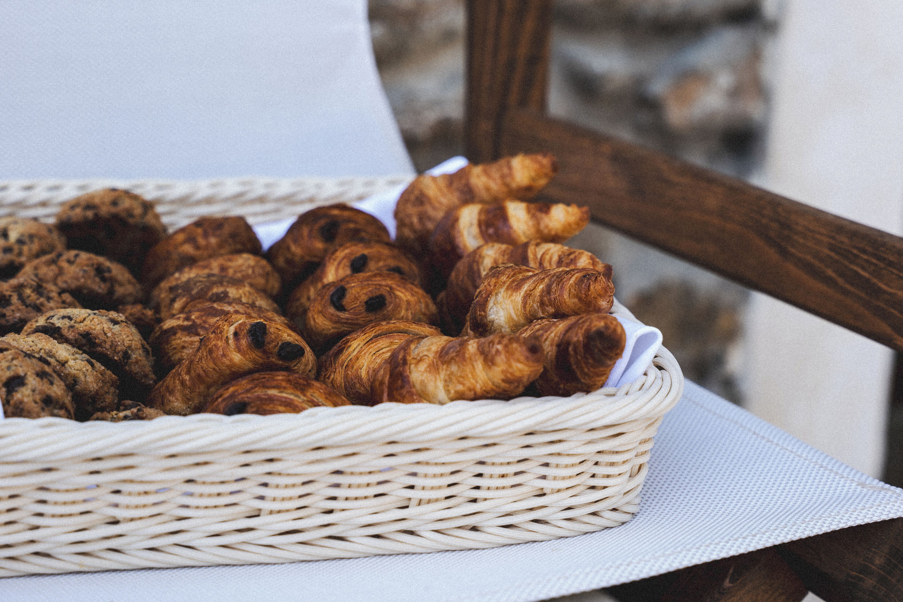 A wicker basket filled with assorted pastries, including croissants and cookies, placed on a white cloth.