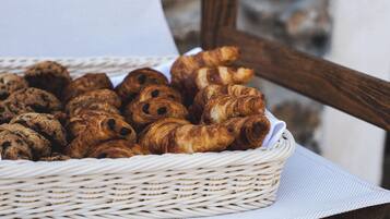 Un panier en osier rempli de diverses pâtisseries, notamment des croissants et des biscuits, posé sur un tissu blanc.
