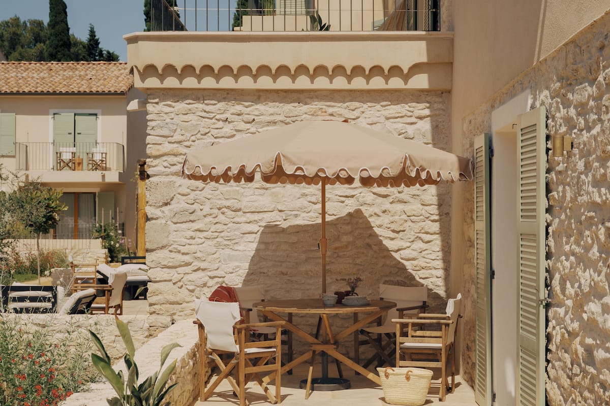 Un patio de piedra con una mesa y sillas, una sombrilla de madera y una pared de piedra.
