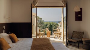A bedroom with a bed, a balcony with a table and chairs, and a view of the outdoors.