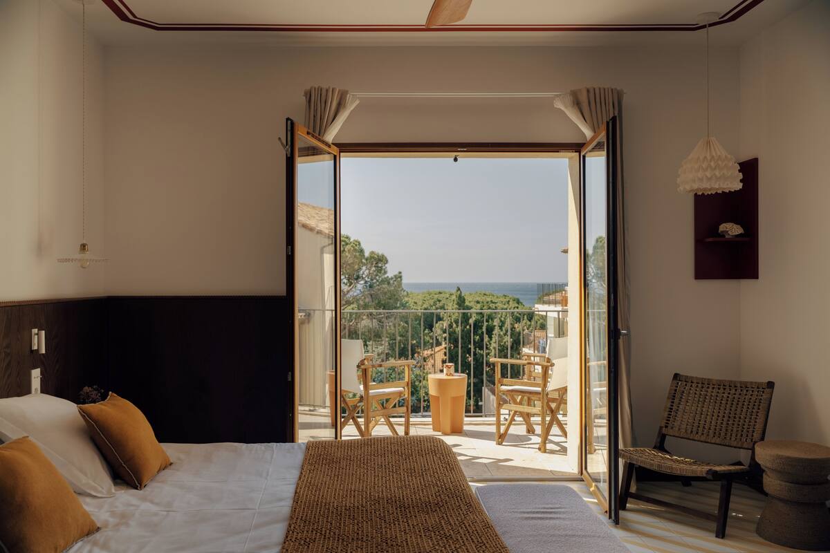 Un dormitorio con cama, un balcón con mesa y sillas, y vista al exterior.