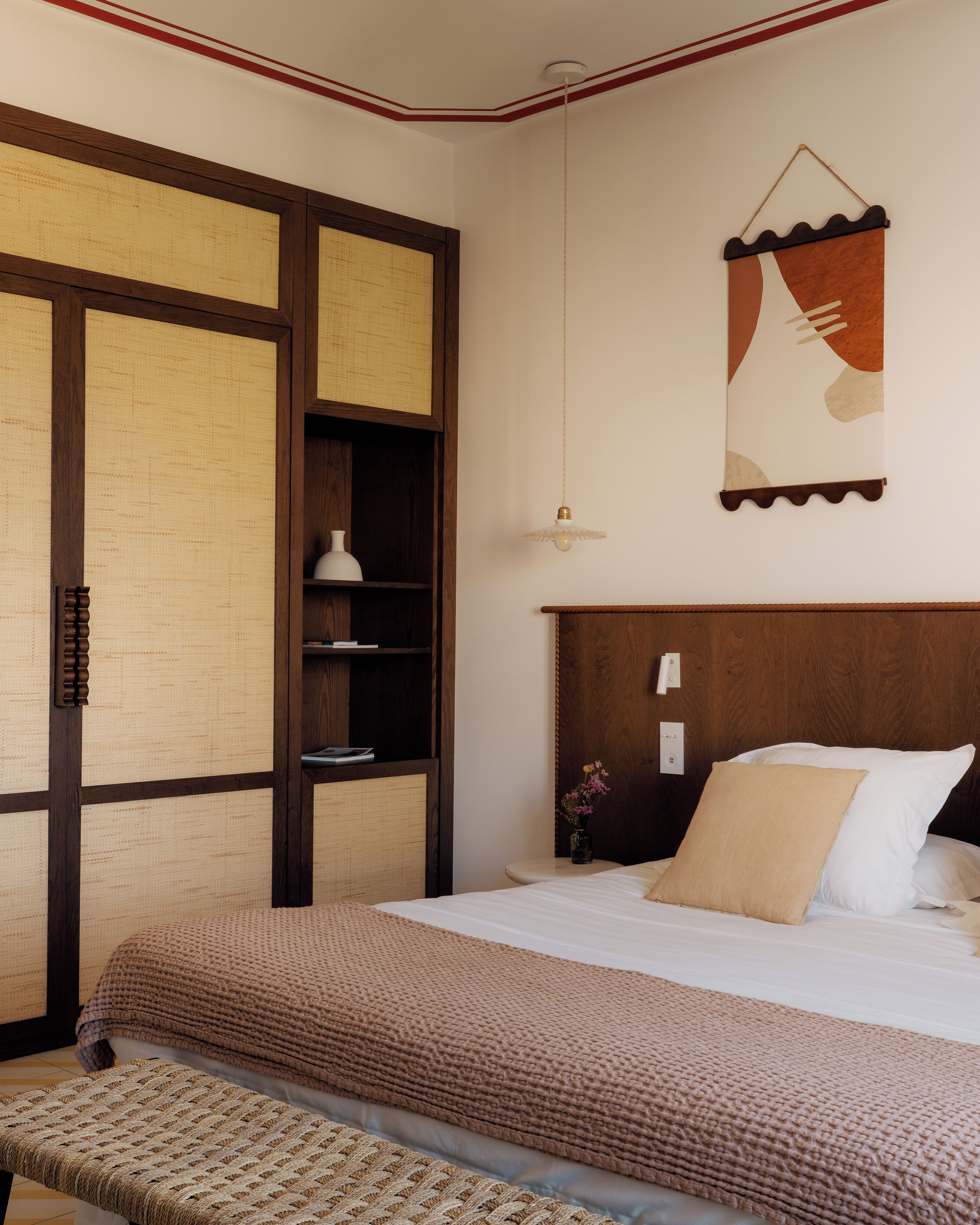 Un dormitorio con una cama grande, cabecera de madera, mesita de noche con lámpara y una obra de arte colgada en la pared.