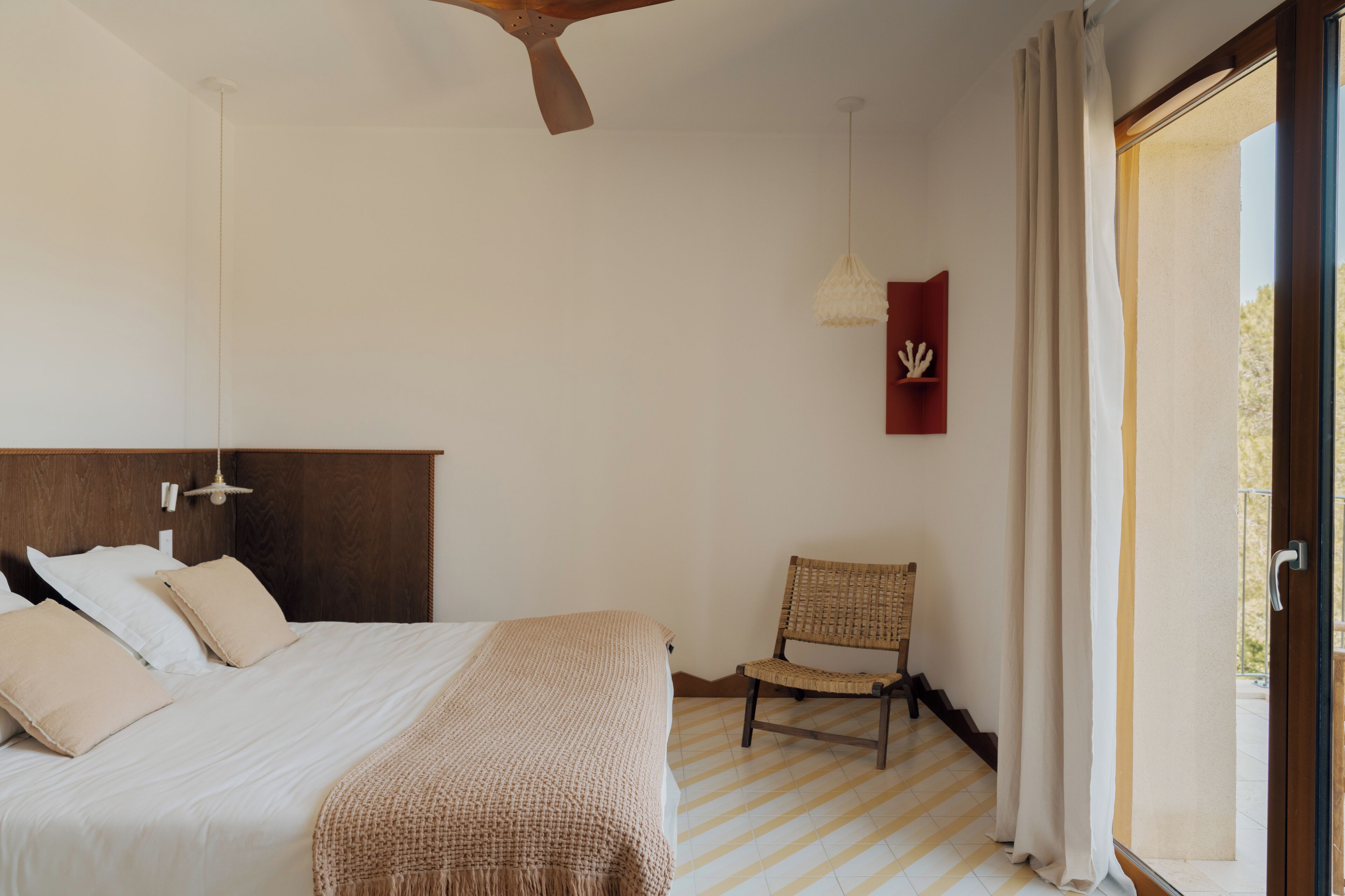 Un dormitorio con cama, una silla, ventilador de techo, luz en la pared y vista por una puerta.