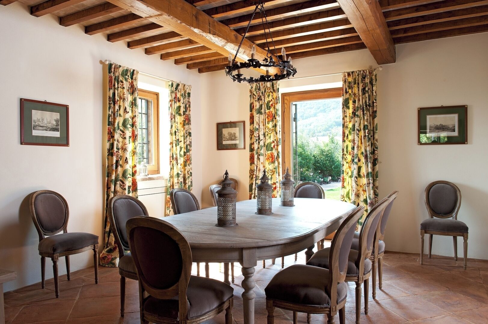 Una sala da pranzo con un tavolo di legno, sei sedie, tende floreali e un lampadario.