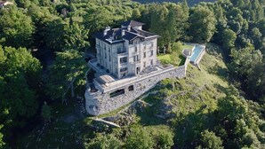 A large, multi-story stone building with a swimming pool, surrounded by lush greenery and hills. - Villa Oltre Le Nuvole - Luxury villa with lake views (Pigra)