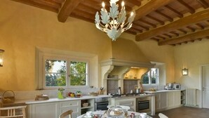 A spacious kitchen with a central island, wooden chairs, and a dining table set for a meal. - Villa Melissa - Stunning Tuscan Villa With Pool (Roccastrada)