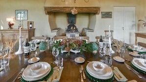 A dining table set for a meal with a chandelier above, a fireplace in the background, and a rustic wooden ceiling. - Villa Melissa - Stunning Tuscan Villa With Pool (Roccastrada)