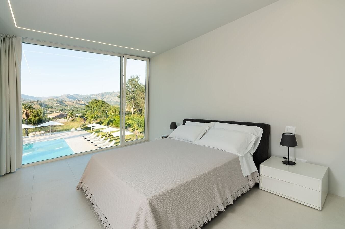 Ein Schlafzimmer mit einem großen Bett, einem Nachttisch und Blick auf einen Pool und Berge.