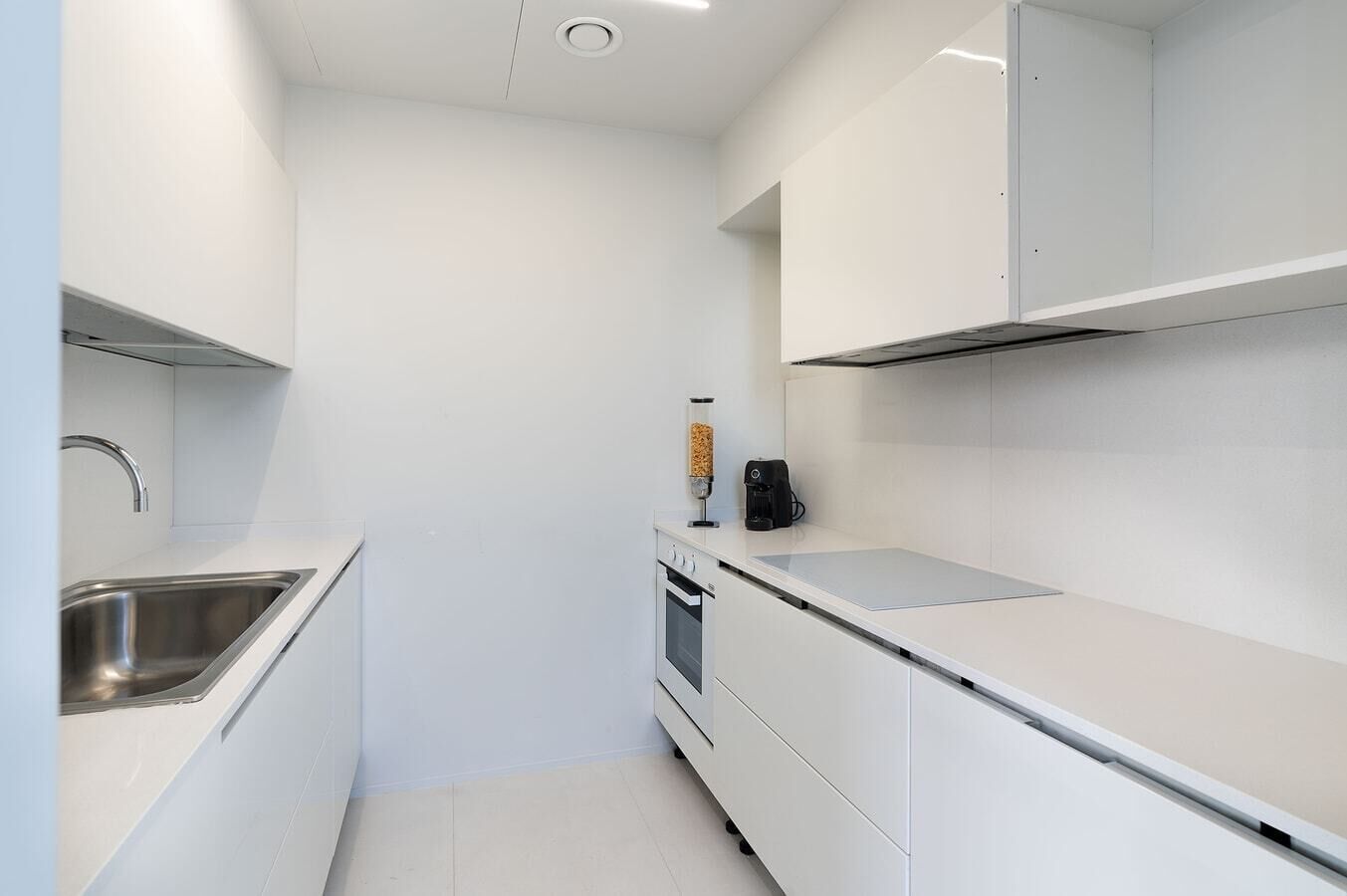 A modern kitchen with white cabinetry, a stainless steel sink, and a coffee machine.