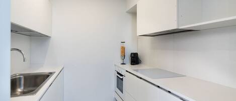 A modern kitchen with white cabinetry, a stainless steel sink, and a coffee machine.