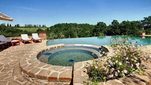 Een rond bubbelbad omringd door stenen zitplaatsen en een zwembad.