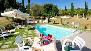Una piscina con sillas de descanso y sombrillas, rodeada de vegetación y árboles.