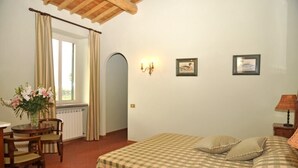 A bedroom with a checkered bedspread, a wooden chair, a table with a vase of flowers, and a window with curtains. - Villa Maria - Countryside villa with a private pool (Magliano Sabina)