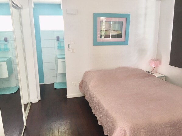Une chambre à coucher avec un lit, une table de chevet, une lampe fixée au mur et un tableau encadré.