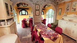 A dining area with a long table set for a meal, arched brick walls, and a view through large windows. - Villa Luna - Umbrian farmhouse with private pool (Castiglione del Lago)