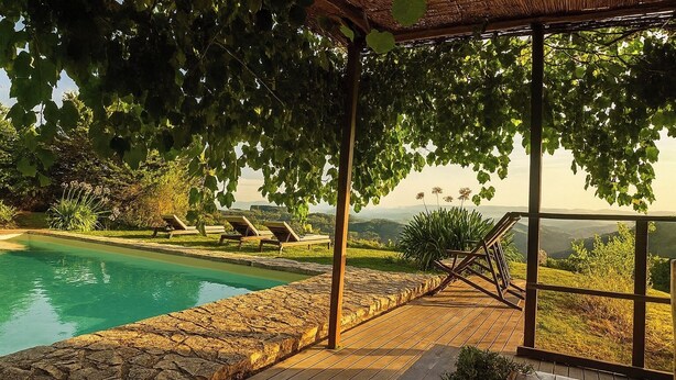 Ein Poolbereich mit Pergola, Liegestühlen und Blick auf die Landschaft.