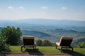 Two wooden lounge chairs facing a scenic view of rolling hills and a valley.