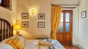 Ein Schlafzimmer mit Bett, Nachttisch, Lampe, einem Fenster mit Vorhängen und gerahmten Bildern an der Wand.