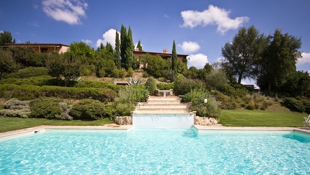 Une piscine à l’eau d’un bleu cristallin, entourée d’une végétation luxuriante et accessible par un escalier en pierre menant à un bâtiment.