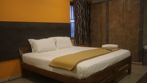 A neatly made bed with white linens and a mustard-colored throw blanket, a wooden headboard, and a wardrobe with a wavy curtain. - Hotel Sikara Kumbakonam (Kumbakonam)