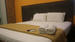 A neatly made bed with white linens, a brown bedspread, and two rolled towels. A remote control is placed on the bed. - Hotel Sikara Kumbakonam (Kumbakonam)