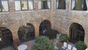 Ein Innenhof mit Steinmauern, Bogenfenstern und Außenbestuhlung.