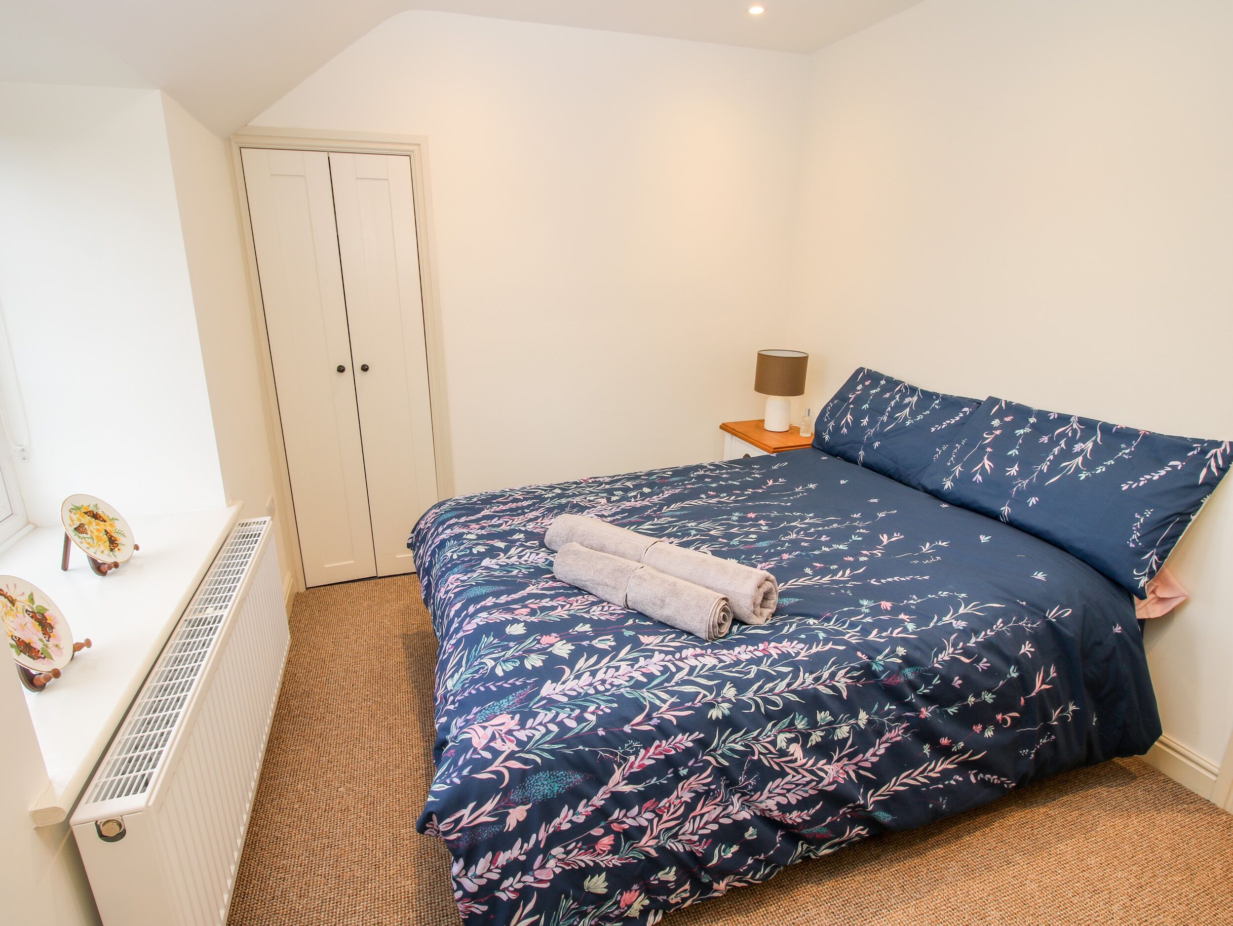 Une chambre à coucher comprenant un lit, une table de chevet, une lampe, un radiateur et une armoire.