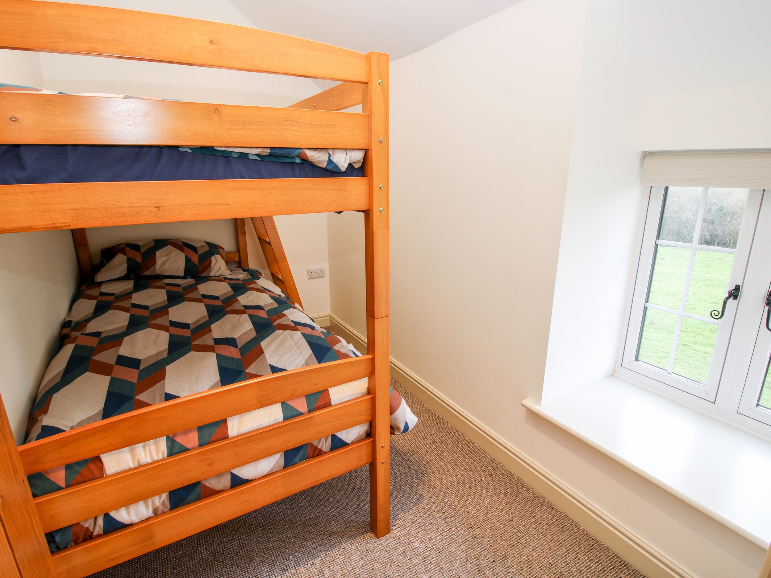 A bunk bed with a geometric-patterned bedspread in a room with a window and carpeted floor.