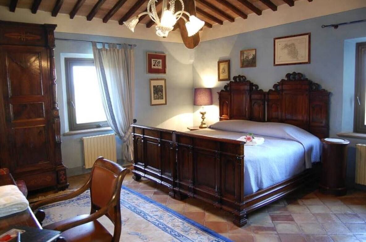 A bedroom with a large bed, wooden furniture, a chandelier, and a window with curtains.