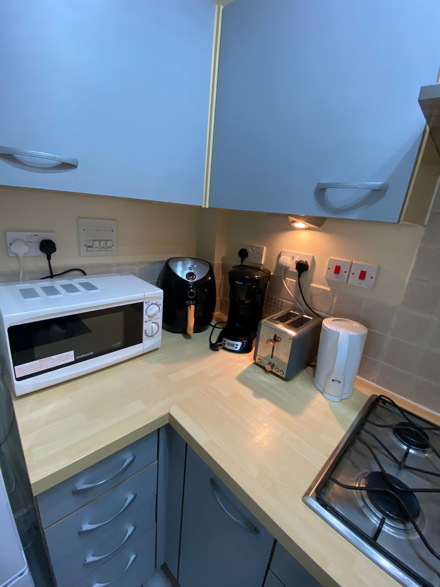 A compact kitchen with a microwave, coffee maker, toaster, and gas stove.