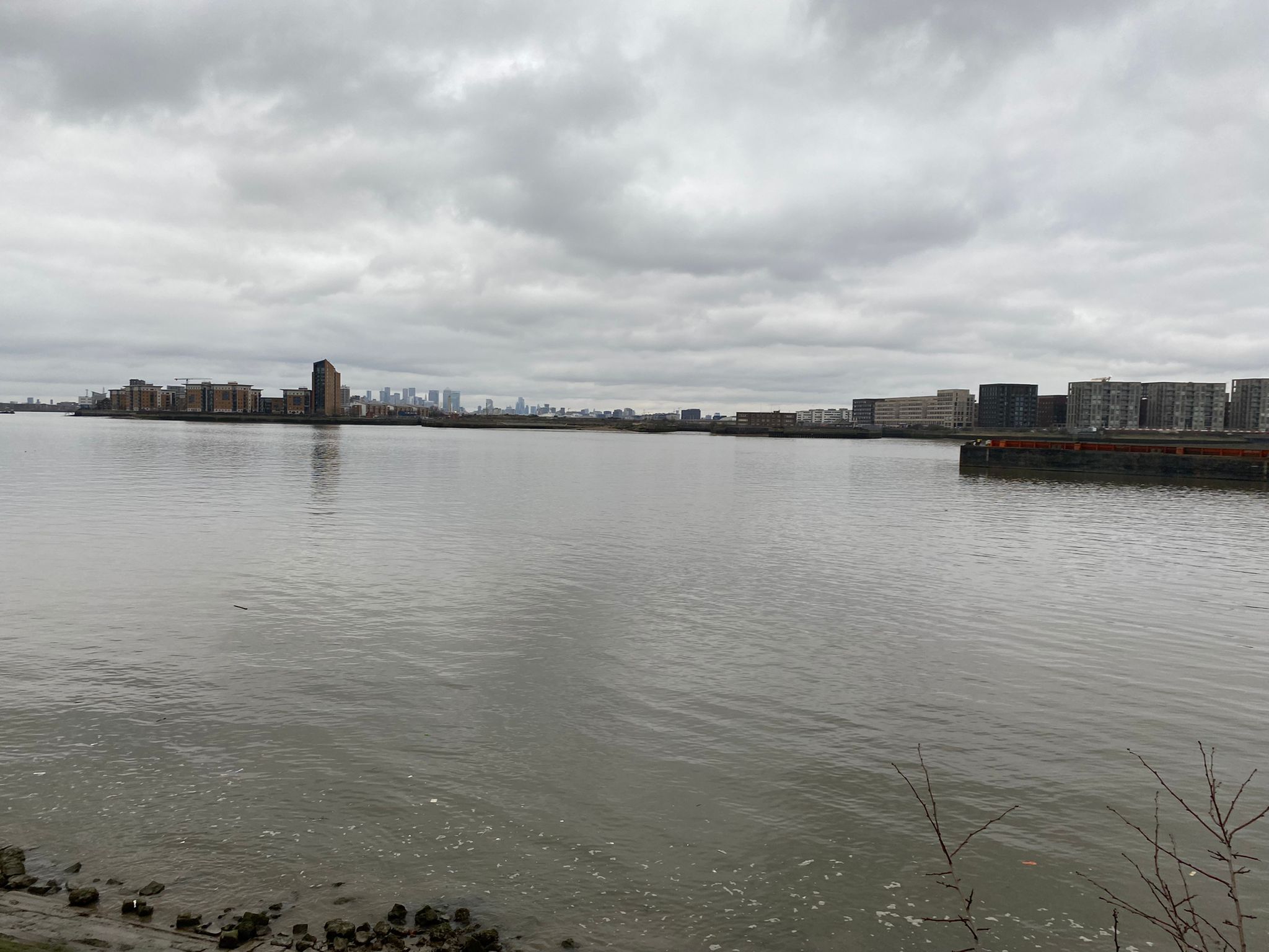 Uitzicht op het water met gebouwen aan de overkant, een steiger en een bewolkte lucht.