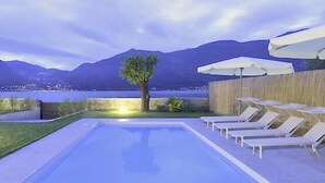Une piscine entourée d’une clôture en bois, agrémentée de chaises longues et de parasols, et offrant une vue sur les montagnes.