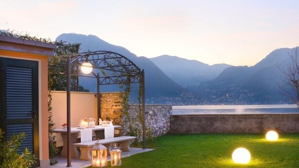 Une terrasse avec une table dressée pour le repas, un mur en pierre et une vue sur les montagnes et un lac.