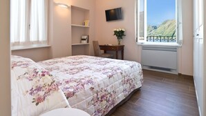Une chambre à coucher comprenant un lit, un bureau, une chaise, un téléviseur et une fenêtre donnant sur des collines.
