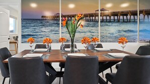 En spiseplads med udsigt til havet og en mole. Der er seks stole, et træbord og en vase med blomster.