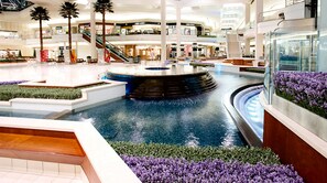 A spacious indoor atrium with a central water feature, multiple levels, and a variety of retail stores.