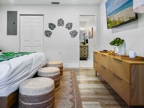 A bedroom with a bed, a wooden dresser, and a view of a beach through a window.
